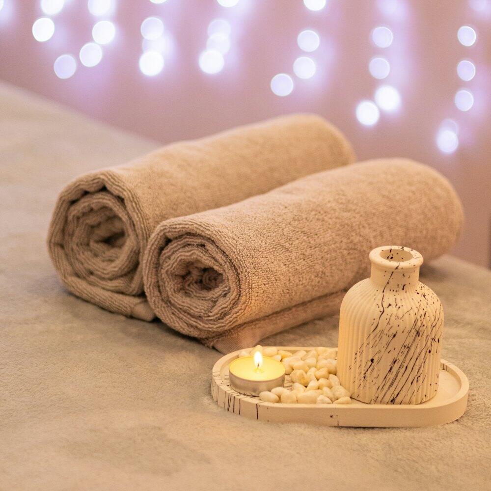Rolled beige towels and a small lit candle on a spa treatment table